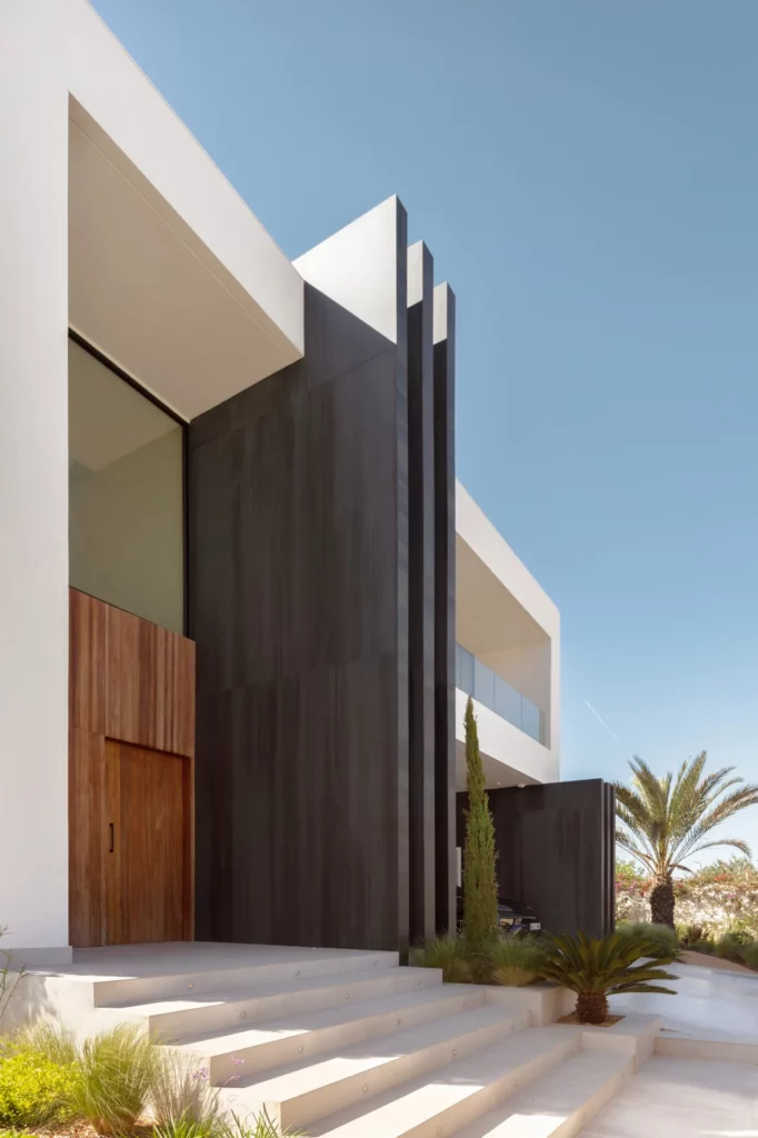 Acceso a villa contemporánea en Ibiza con puerta de madera, escalones y fachada oscura