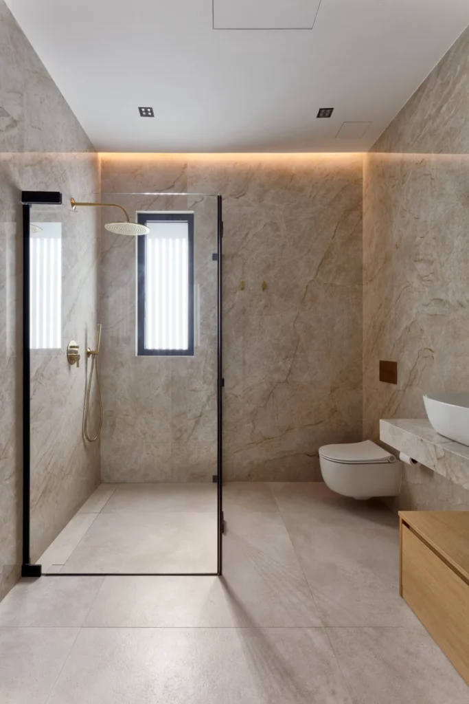 Baño de villa en Ibiza con ducha de cristal, revestimiento beige e iluminación indirecta